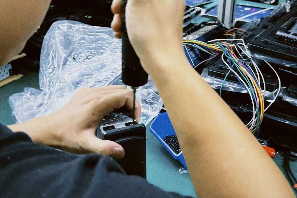 Seorang teknisi sedang melakukan pengujian di meja kerja terhadap panel instrumen digital khusus kendaraan selama proses pemeriksaan garansi